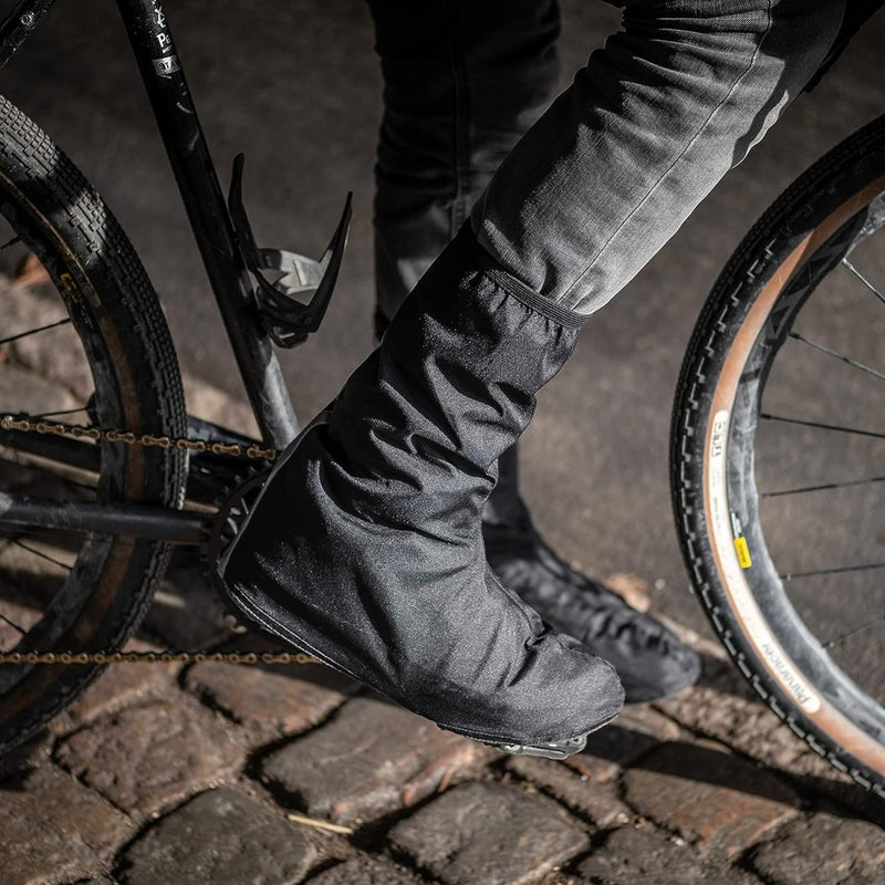Laad afbeelding in Galerijviewer, Close-up van een fietser die &quot;Regenoverschoenen voor fietsers: blijf droog en stijlvol&quot; draagt op geplaveide stoep ter bescherming.
