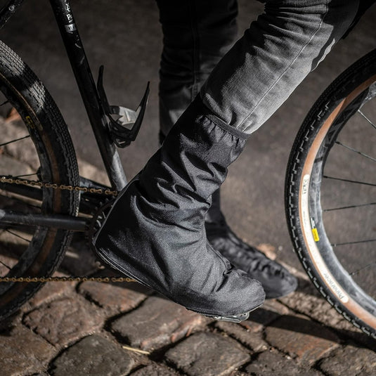 Close-up van een fietser die "Regenoverschoenen voor fietsers: blijf droog en stijlvol" draagt op geplaveide stoep ter bescherming.