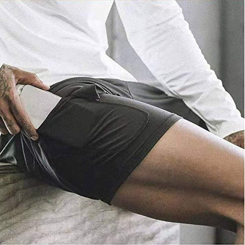 Laad afbeelding in Galerijviewer, De persoon zit comfortabel in een zwarte heren 2-in-1 short met een smartphone deels in de zak. De shorts hebben een geïntegreerde compressieshort, gemaakt van sneldrogend materiaal, en zijn perfect te combineren met hun stijlvolle witte longsleeve shirt.
