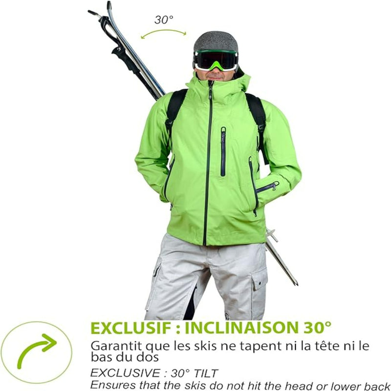 Load image into Gallery viewer, Iemand draagt een groene jas en een witte broek en draagt vakkundig de ski&#39;s in een hoek van 30 graden met behulp van de Skiback, zodat hij zijn handen vrij heeft en de ski&#39;s comfortabel kan dragen.
