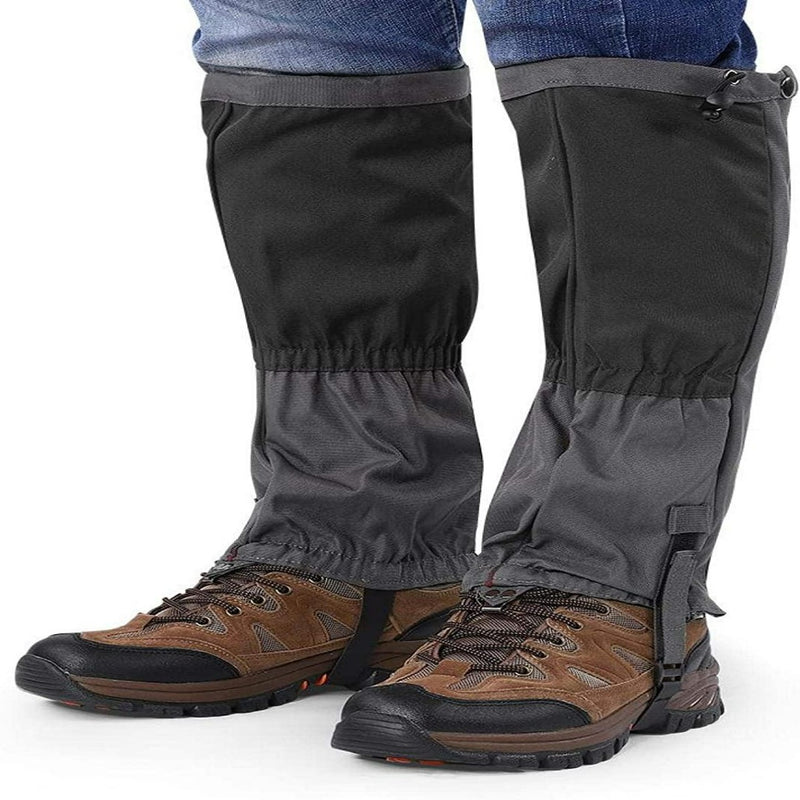 Laad afbeelding in Galerijviewer, Een persoon draagt wandelschoenen met Ontdek het ultieme comfort en bescherming met onze sneeuw gamaschen voor volwassenen in strak zwart en grijs over een blauwe broek.
