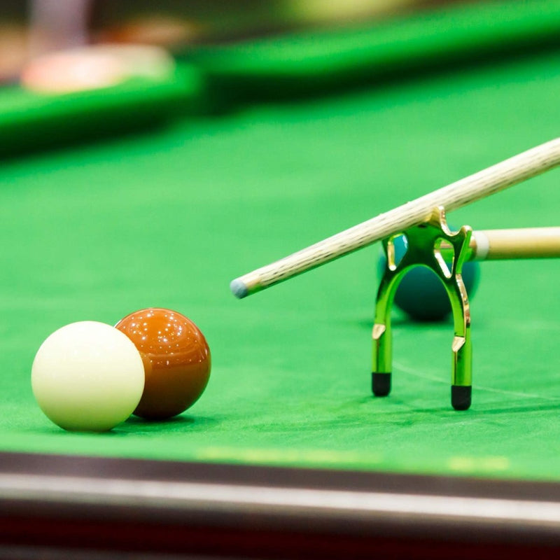 Load image into Gallery viewer, De &quot;Snooker tafelsteunen: verbetering je spel met precisie en stabiliteit met deze keubruggen&quot; maakt deel uit van een elegante accessoireset en rust op een koperen keusteun, klaar om een rode bal te slaan in de buurt van de witte speelbal op de groene tafel.
