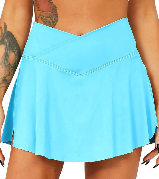 Ze dragen een "Tennisrok met broek: de perfecte sportoutfit voor elke vrouw" in lichtblauw met een asymmetrisch design en praktische zakken, waarbij de tatoeages op de linkerarm en zwartgelakte nagels goed zichtbaar zijn.