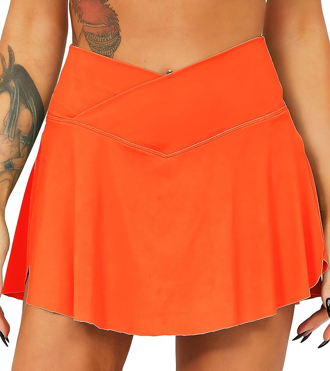 Laad afbeelding in Galerijviewer, Een persoon draagt de Tennisrok met broek, een oranje wikkelrok met een flatterende pasvorm, voorzien van praktische zakken. Op de arm is een tatoeage zichtbaar.
