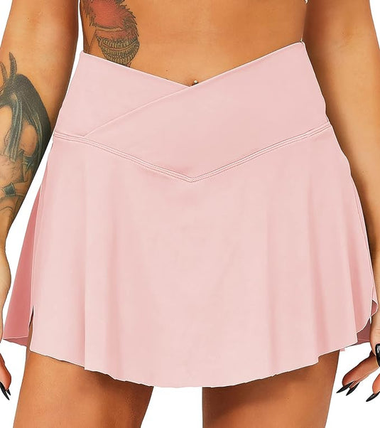 Een persoon in een Tennisrok met broek, lichtroze met wikkelontwerp, die maximale bedekking en ondersteuning biedt, toont zijn expressieve armtatoeages.