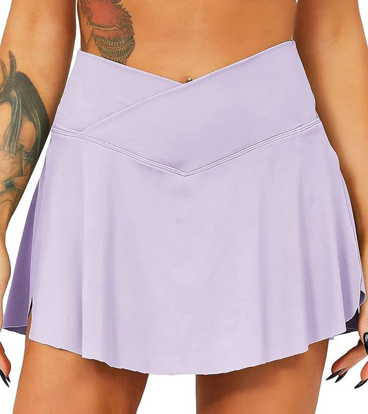 Een persoon draagt een lichtpaarse rok met hoge taille en een gekruiste voorkant, die doet denken aan de "Tennisrok met broek: de perfecte sportoutfit voor elke vrouw", waardoor tatoeages op de rechterarm zichtbaar zijn.