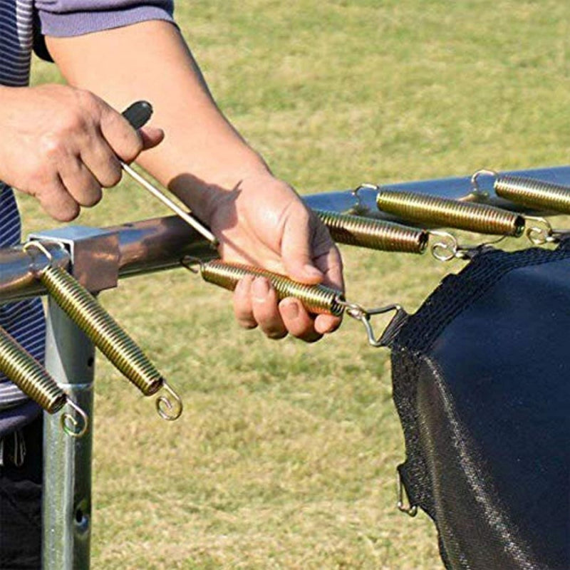 Laad afbeelding in Galerijviewer, Een persoon gebruikt vakkundig een T-haak veertrekker, het perfecte gereedschap voor het installeren van trampolineveren op het frame dat in een grasveld is opgesteld.
