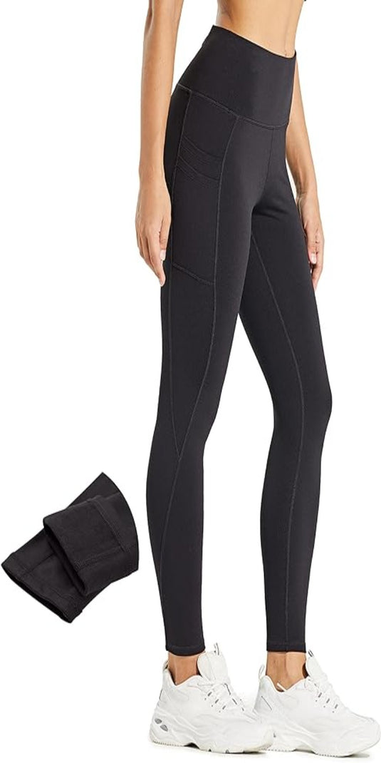 Een persoon draagt een waterafstotende zwarte legging met hoge taille en witte sneakers vanaf de zijkant. Ernaast ligt een opgevouwen paar Warm, comfortabel en waterafstotend: de perfecte thermische legging voor dames in zwart.