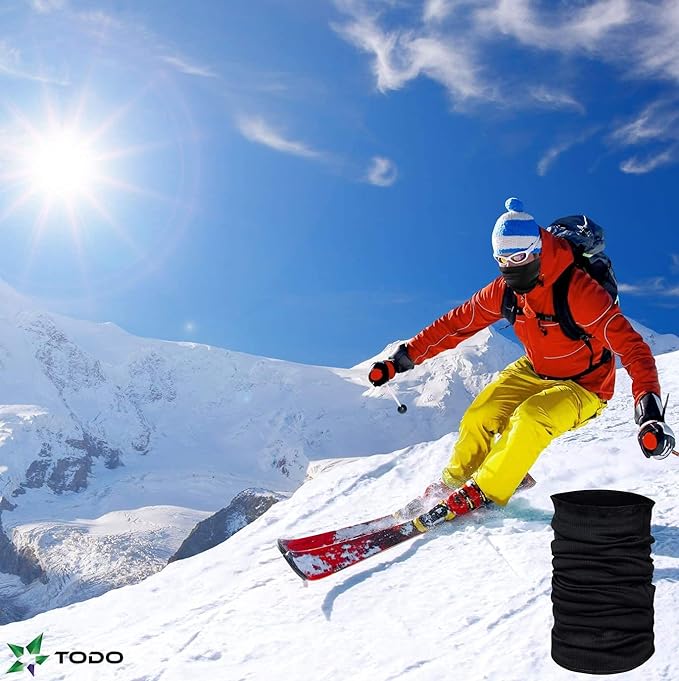 Laad afbeelding in Galerijviewer, Een skiër in een gele broek, rode jas en blauwgestreepte hoed racet bergafwaarts op een besneeuwde berg onder een helderblauwe lucht. Een zwarte gaiter gemaakt van Trotseer de kou met onze universele colsjaal: warmte en comfort in één! gluurt naar buiten en versterkt zijn multifunctionele stijl op de piste.
