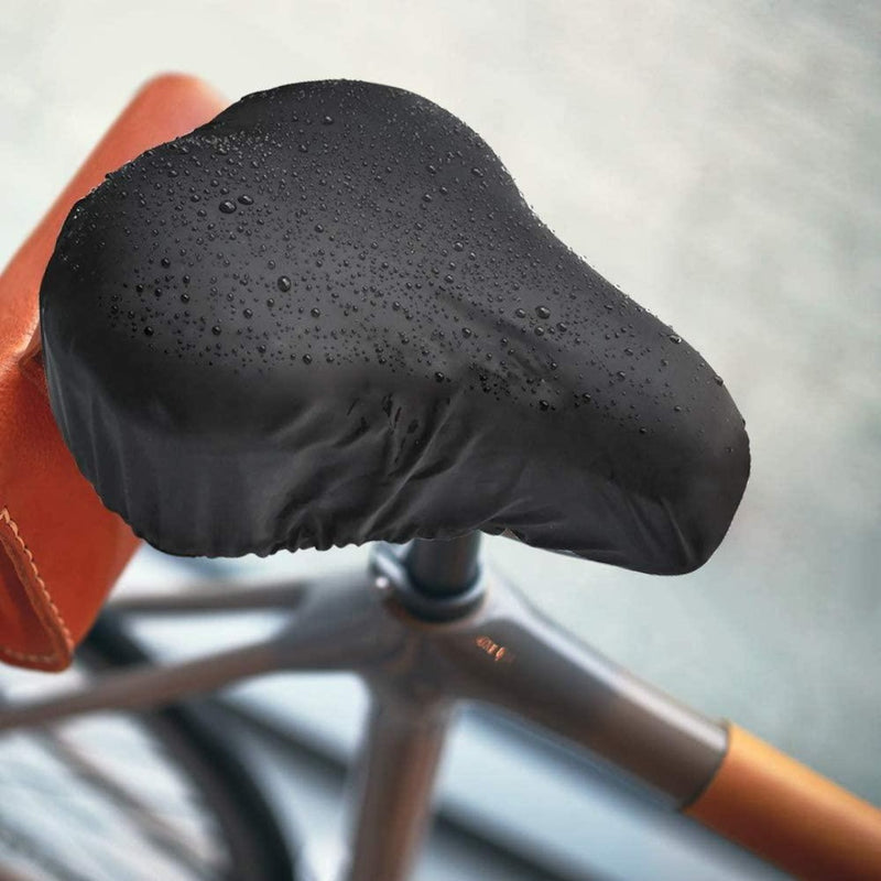 Load image into Gallery viewer, De Geniet van comfortabel fietsen zadelhoes, met zijn strakke zwarte hoes, glanst onder waterdruppels en toont zijn waterdichte design. Een vleugje bruin leer voegt elegantie toe, waardoor het perfect is voor stadsfietsers die op zoek zijn naar stijl en functionaliteit, terwijl het moderne fietscomfort belichaamt.
