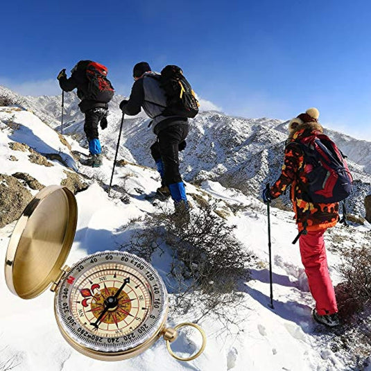 Drie wandelaars met trekkingstokken beklimmen onder een strakblauwe hemel een besneeuwde berg, begeleid door het Happygetfit zakkompas. Een inzetstuk van dit veelzijdige "ontdek de betrouwbare metgezel voor jouw avonturen: het Happygetfit zakkompas voor buiten navigatie" belicht hun avontuurlijke en fitnessreis.